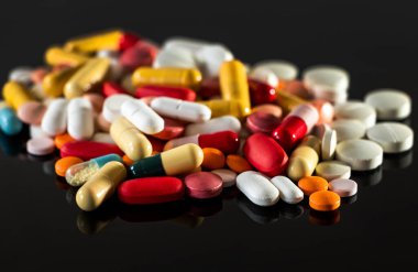 Pile of different medicaments pills, capsules, on black background with reflection