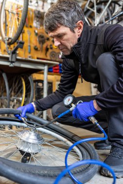 Cycling technician maintaining bike, blowing tires with manual pressure pump in workshop