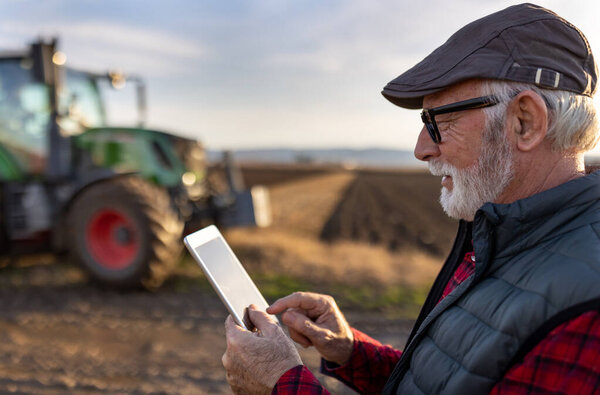 Возбужденный зрелый фермер работает на планшете перед трактором в поле