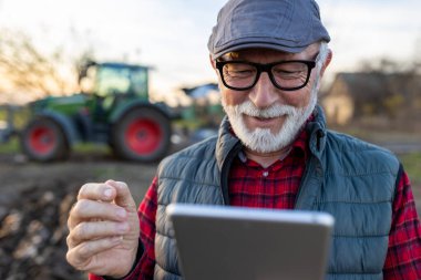 Smiling mature farmer looking at tablet in front of tractor in field