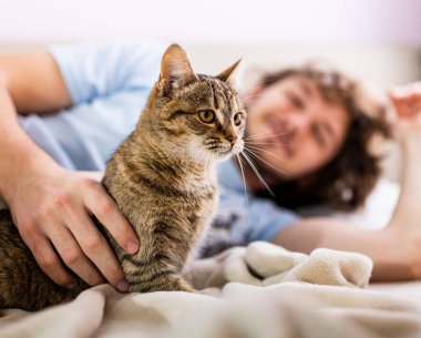 Young man cuddling cute tabby cat in bed