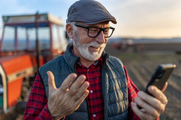 Excited mature farmer talking on mobile phone in front of tractor in field