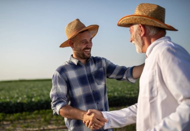 Two farmers shaking hands in field at summer hot day