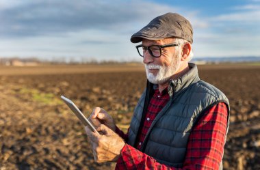 Senior farmer smiling and holding tablet in field in autumn time