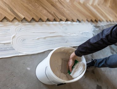 Worker spreading glue with spatula on concrete floor for parquet installation in apartment