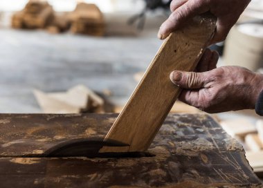 Close up of carpenter's hands holding parquet on circular saw for trimming and installation
