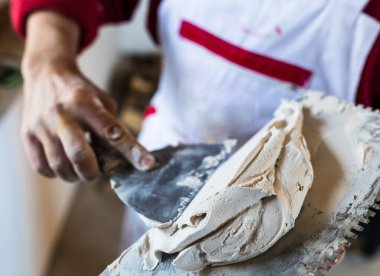 Close up craftsman's hand holding spatula with plaster mass for renovating wall