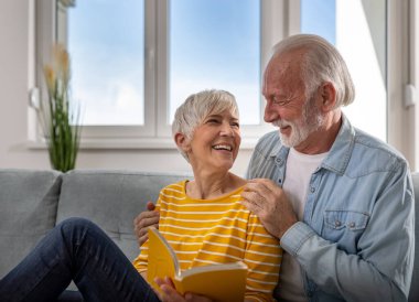 Evdeki kanepede oturup kitap okuyan ve gülümseyen neşeli son sınıf çifti.