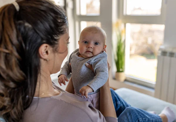 若いお母さんは自宅のソファに座って かわいい新生児を手に持っています 母なる愛 ケアと喜びの概念 — ストック写真