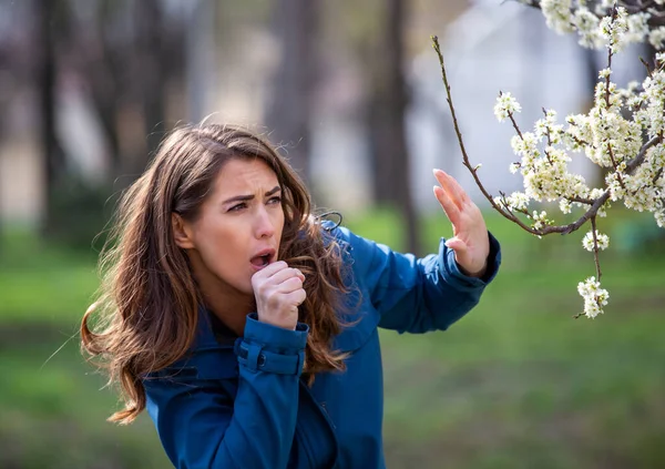 美丽的年轻女子站在开花的树前 因为花粉过敏而感到害怕 — 图库照片