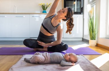 Genç, güzel anne yeni doğmuş bebek uyurken mutfak dolaplarının önünde yoga minderiyle egzersiz yapıyor. Sağlıklı zihinsel ve fiziksel durum kavramı