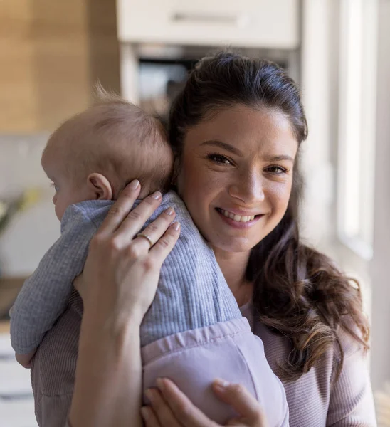 肩に赤ちゃんを抱えている可愛いお母さんの笑顔と 窓の横の家で抱擁で優しい静かな瞬間を楽しむ肖像画 母なる愛 ケアと喜びの概念 — ストック写真