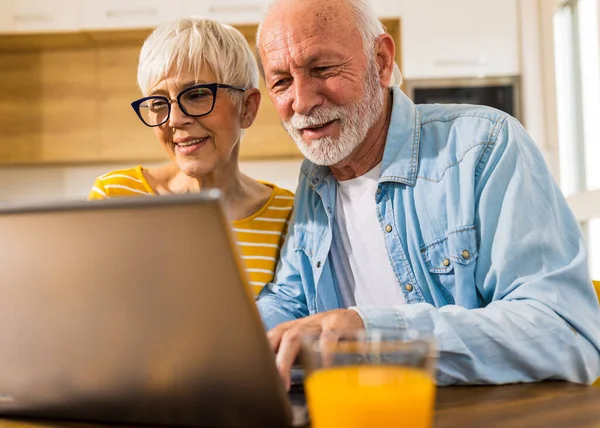 Fröhliches Seniorenpaar Sitzt Esstisch Mit Küche Hintergrund Und Surft Auf — Stockfoto