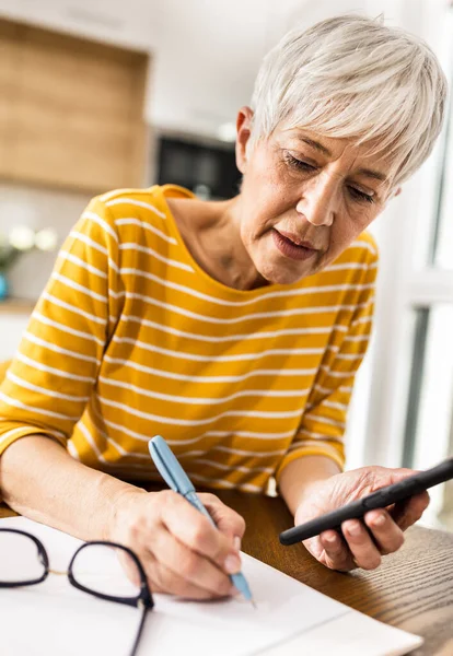 Mature Woman Calculating Household Bills Mobile Phone Writing Costs Savings — Stock Photo, Image