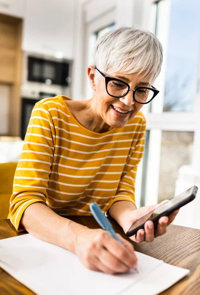 Smiling Mature Woman Calculating Household Bills Mobile Phone Writing Costs — Stock Photo, Image