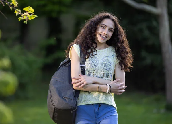 Ładna Dziewczyna Długimi Kręconymi Włosami Trzymająca Plecak Ręce Skrzyżowane Parku — Zdjęcie stockowe