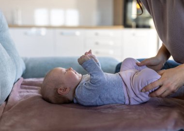 Sevimli yeni doğmuş bebek sırt üstü uzanıyor ve yatakta annesine gülümsüyor.