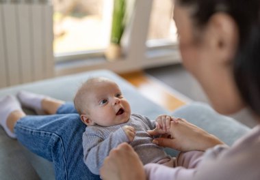 Genç anne evdeki kanepede oturuyor ve kucağında güzel bir bebek, kalçasında gülüyor ve oynuyor. Annelik aşkı, ilgi ve neşe konsepti