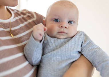 Annesinin kollarında kameraya bakan sevimli bir bebeğin portresi. Annelik sevgisi ve bakım konsepti