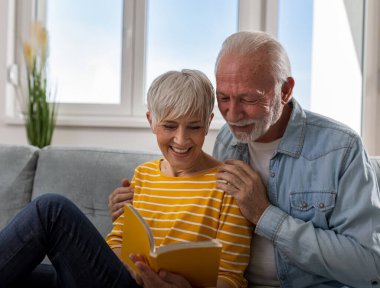 Evdeki kanepede oturup kitap okuyan ve gülümseyen neşeli son sınıf çifti.