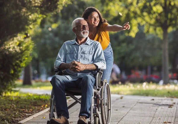 여자가 공원에서 휠체어에 아버지를 산책에 시간을가지고 스톡 사진