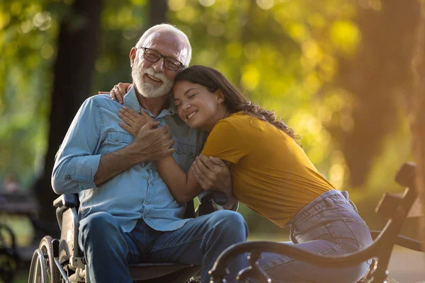 父と娘の幸せな瞬間でした 公園の車椅子で年配の男性を抱きしめている若い女性 障害者と女の子が彼の世話をする老人 ロイヤリティフリーのストック画像