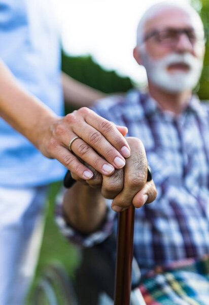 Close up of senior man hand on walking stick with female nursing hand as support and empathy