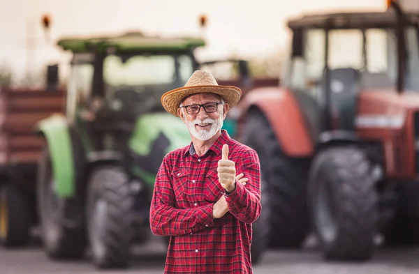 Zufriedener Landwirt Mit Strohhut Steht Zur Erntezeit Vor Zwei Traktoren Stockbild