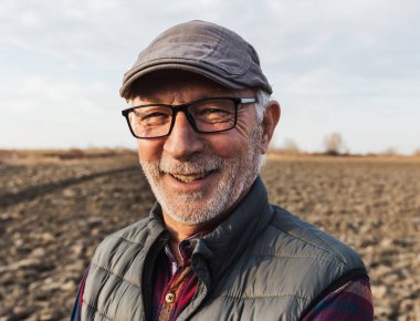 Kış zamanı tarlada duran gözlüklü ve şapkalı kıdemli çiftçinin portresi