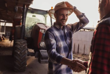 İki genç ve olgun çiftçi anlaşmanın işareti olarak traktör önünde el sıkışıyor..