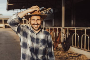 Satisfied farmer holding straw hat in front of young cattle on dairy ranch