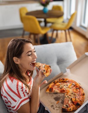 Evdeki rahat oturma odasında, kanepede pizza yiyen güzel bir kadın.