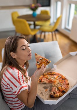 Evdeki rahat oturma odasında, kanepede pizza yiyen güzel bir kadın.