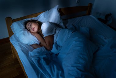 Genç ve güzel bir kadın, sabahları yatakta dinlenirken, odaya güneş ışınları giriyor.