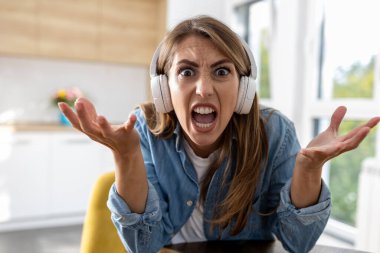 Kızgın kadın kameraya bağırıyor, arka planda mutfağı olan bir video konferans görüşmesi yapıyor.