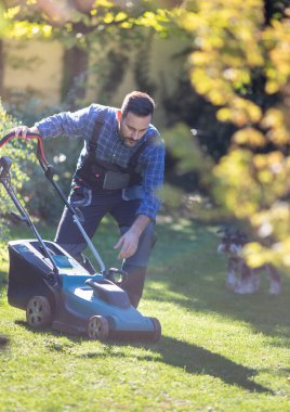 Çim biçme makinesini çalıştıran yakışıklı bir adam arka bahçesinde motoru olan, sonbaharda bahçeyle ilgilenen,