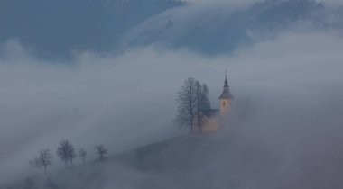 Landscape of Slovenian Alps with St. Primoz church, landmark surrounded with dense fog clipart