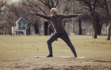Son sınıf öğrencisi yoga yapıyor. Savaşçıya parkta poz veriyor. Kollarını ve bacaklarını açıyor. Meditasyon ve sağlıklı yaşam tarzı konsepti