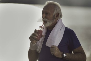Antrenmandan sonra sakallı yaşlı adam samanla taze meyve suyu içiyor.