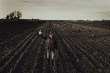 Bir elinde dizüstü bilgisayarı olan kıdemli çiftçinin hava görüntüsü. Sonbaharın sonlarında balya işleminden sonra sahada birini selamlamak için el sallıyor.