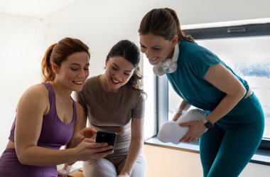Üç kız spor salonunda spor yapmak için akıllı telefonu seve seve incelerler. Gün boyunca kapalı bir alanda.