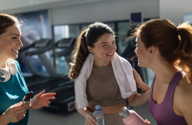 Spor salonunda dinlenen, spor yaptıktan sonra konuşan, su ve protein barlarıyla dolu şişeleri tutan üç neşeli genç kadın. Spor ve sağlıklı yaşam tarzı kavramı