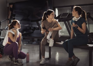 Spor salonunda dinlenen, spor yaptıktan sonra konuşan ve protein barları tutan üç neşeli genç kadın. Spor ve sağlıklı yaşam tarzı kavramı