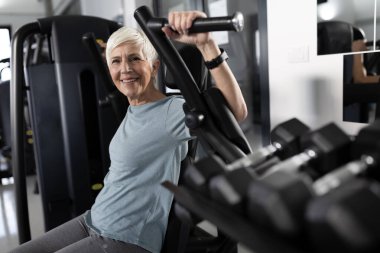 Kadın katılımcı spor salonunda çalışıyor, güçlü eğitim ekipmanları kullanıyor. Egzersiz sırasında odaklanmış ve kararlı görünüyor.