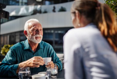 Beyaz sakallı yaşlı bir adam güneşli bir kafede arkadaşıyla kahve içerken gülümsüyor. Dostça bir sohbete giriştiler..