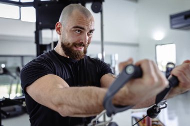 Spor salonundan terleyen, kol egzersizi için ekipman kullanan kendine güvenen erkeklerin yakın çekimi.