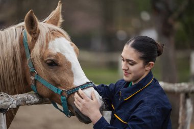 Kadın seyis atlarını okşarken gülümseyerek çiftlikte huzurlu bir sabah geçiriyor.. 