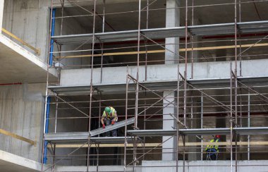 İnşaat işçileri gündüz saatlerinde bir inşaat alanında inşaat iskelesi kuruyorlar.