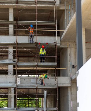 İnşaat işçileri gündüz saatlerinde bir inşaat alanında inşaat iskelesi kuruyorlar.