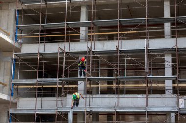 İki erkek işçi, gündüz saatlerinde bir inşaat sahasında yapı iskelesi kuruyor.